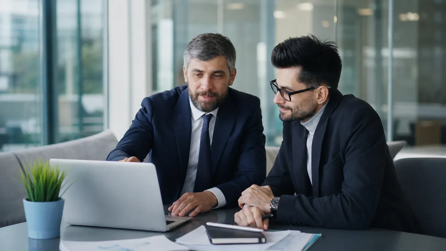 Two colleagues reviewing work together at a laptop in an office